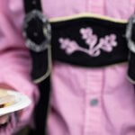 Close up of person in pink and black Oktoberfest outfit holding two small plates of sausage